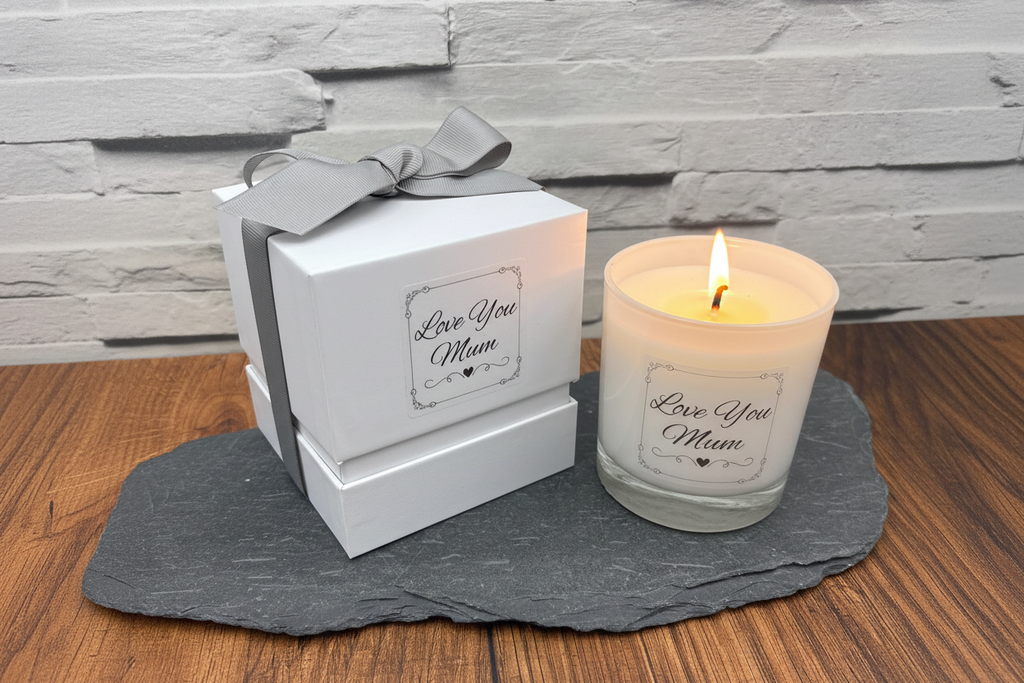 Candle with 'Love You Mum' message next to a gift box on a wooden surface.