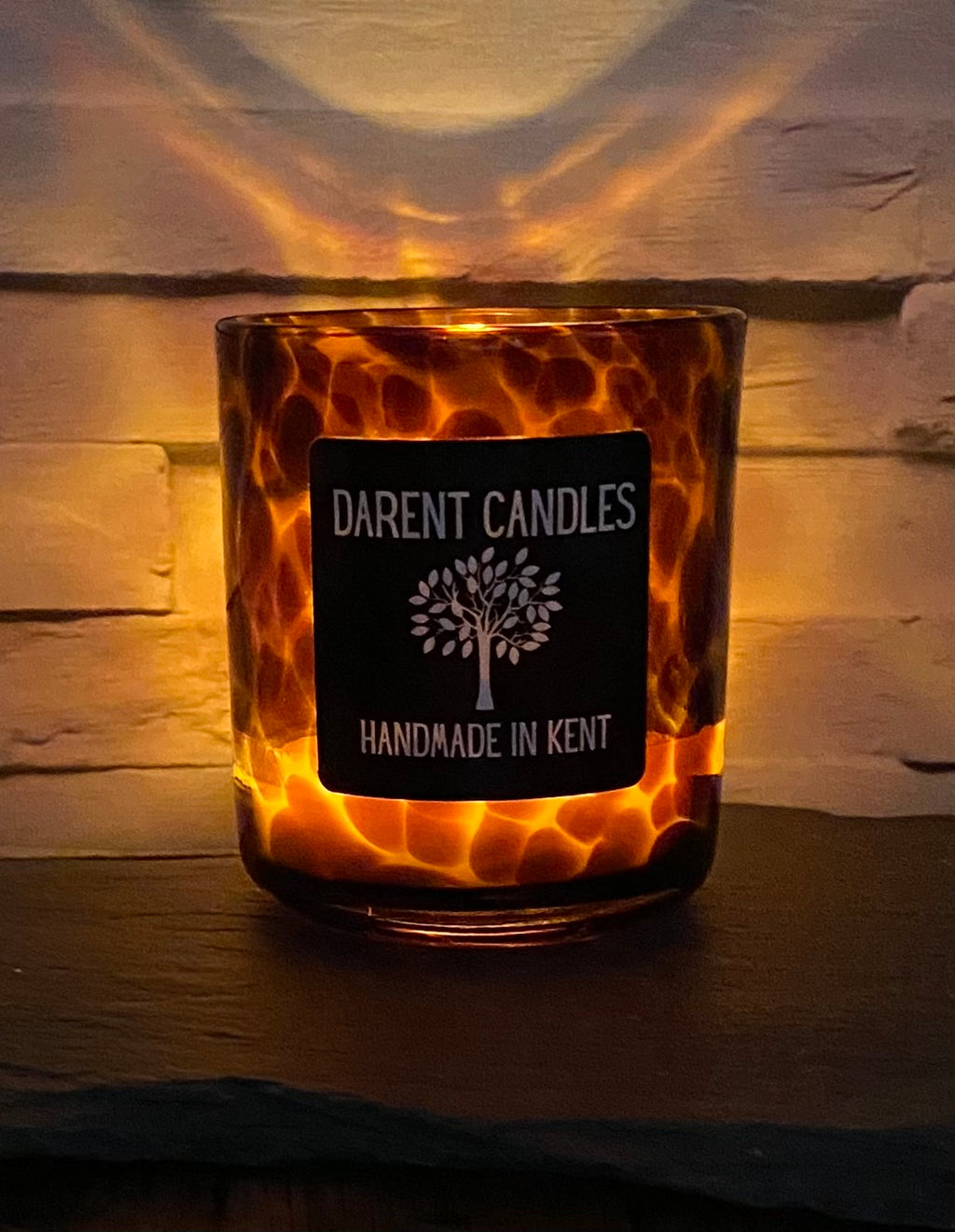 Candle in a tortoiseshell-patterned holder with 'Darent Candles' label on a wooden surface.